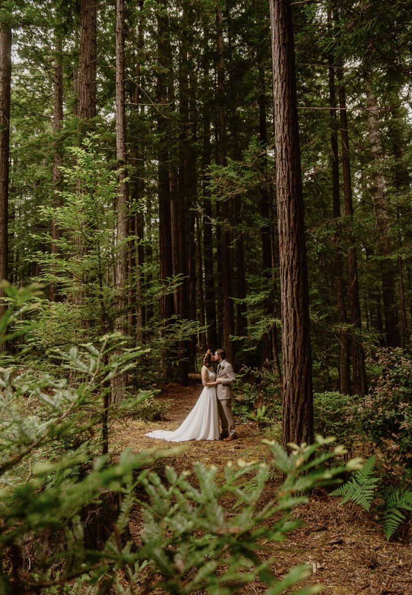 A couple embraces in a kiss in the redwood forest on their wedding day. The groom wears a beige suit and the bride wears a white sleeveless dress with a train and a flower crown. Learn how to write wedding vows with prompts and emotional guidance to help you feel clear, calm, and connected—without sounding cliché.
