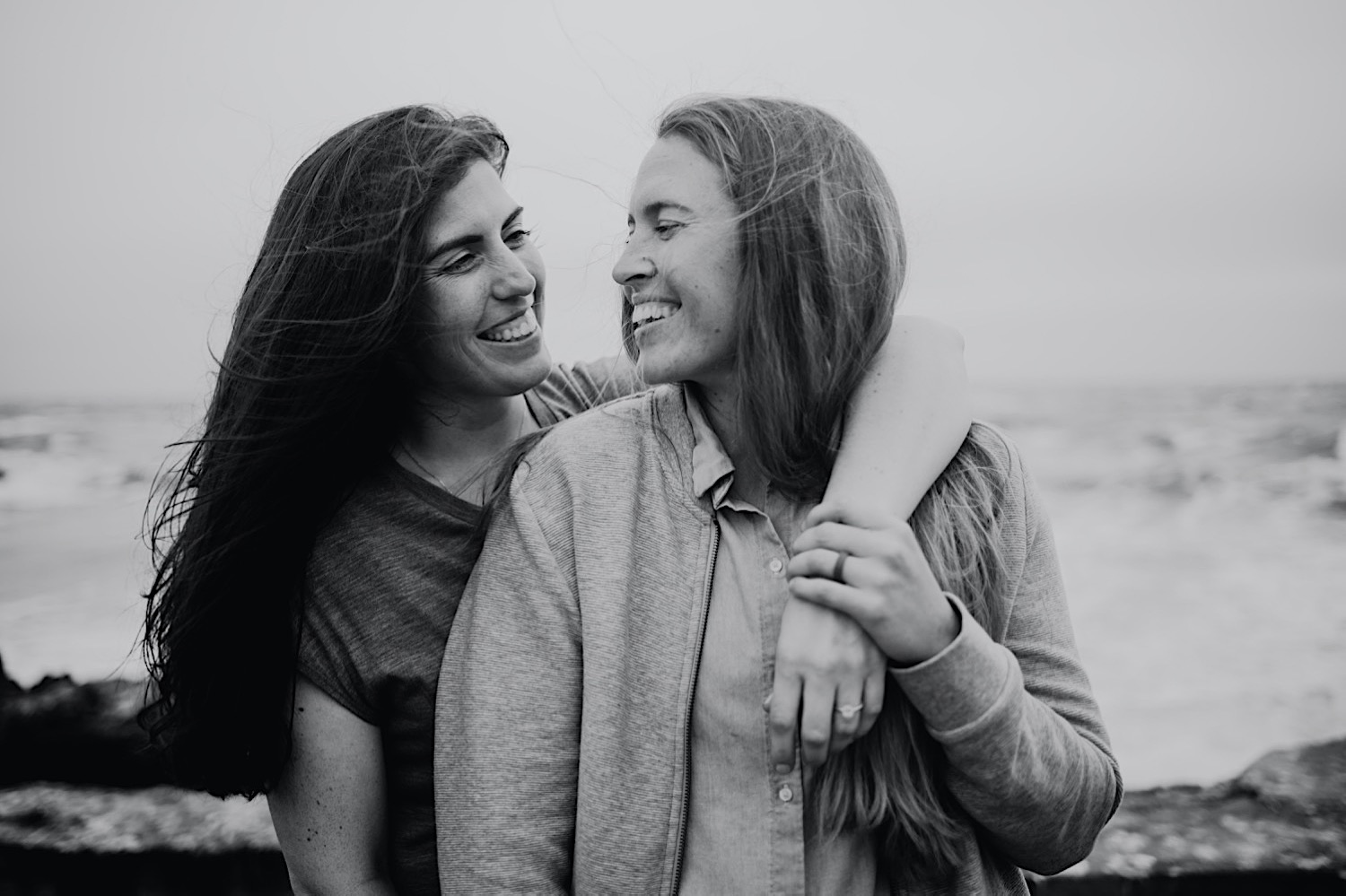 Two women with long hair are smiling and laughing while looking at each other and embracing. One has her arm around the other's shoulder.

They stand on the ruins of the Sutro Baths in San Francisco for their engagement session. Head to this post to see more photos from my bucket list location!