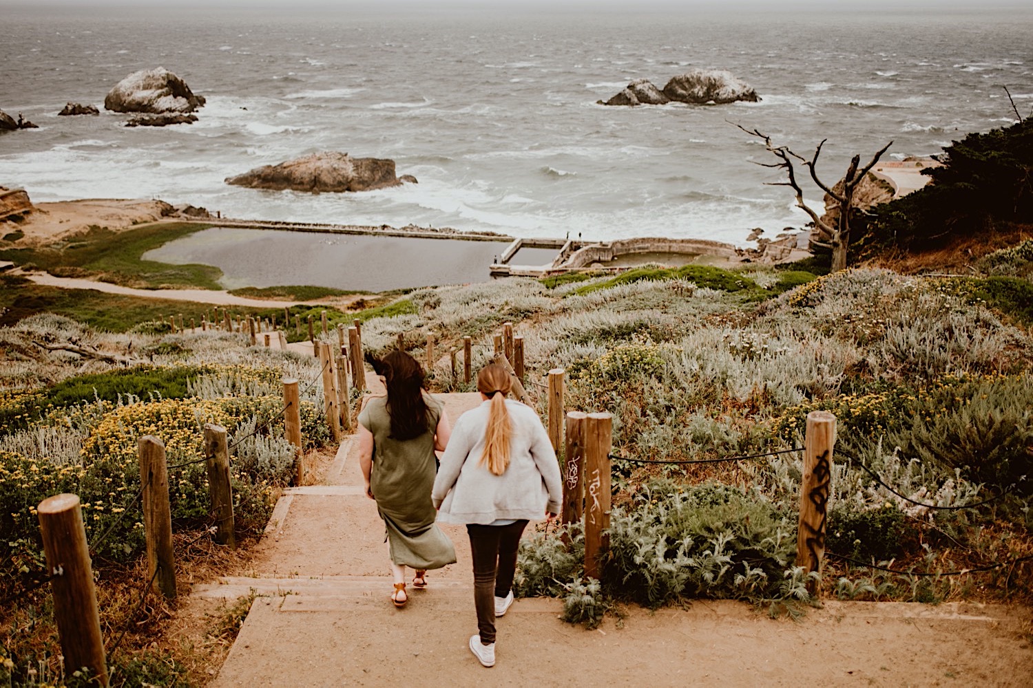 Two women with long hair walk down the stairs to the ruins of the Sutro Baths in San Francisco for their engagement session. Head to this post to see more photos from my bucket list location!