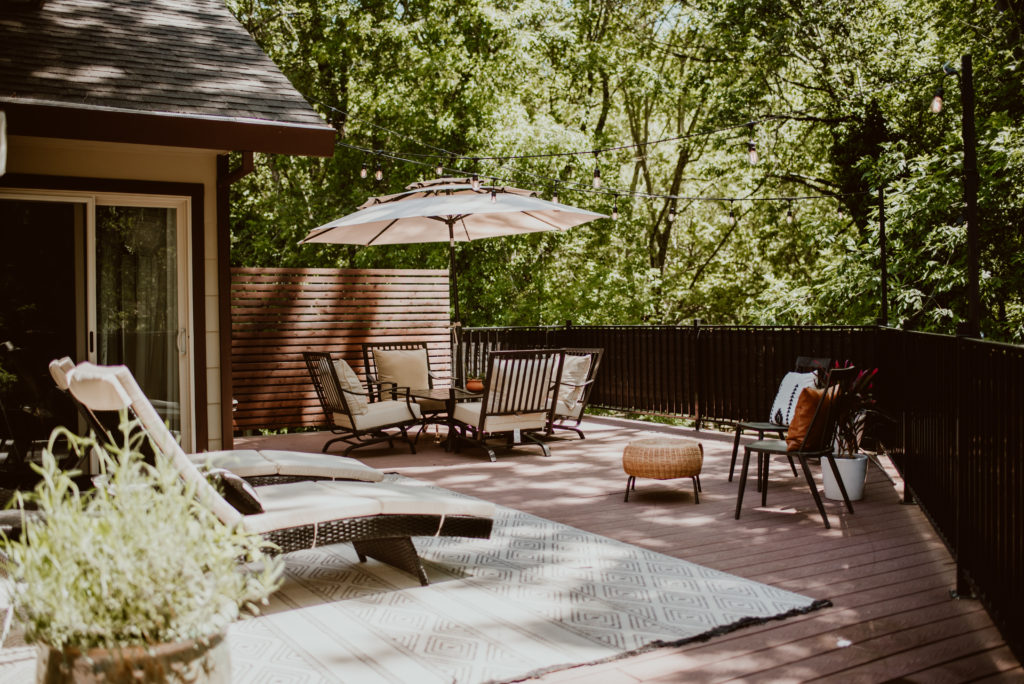 A backyard deck is shown with chaise lounges and numerous chairs and umbrella, ready for summer.