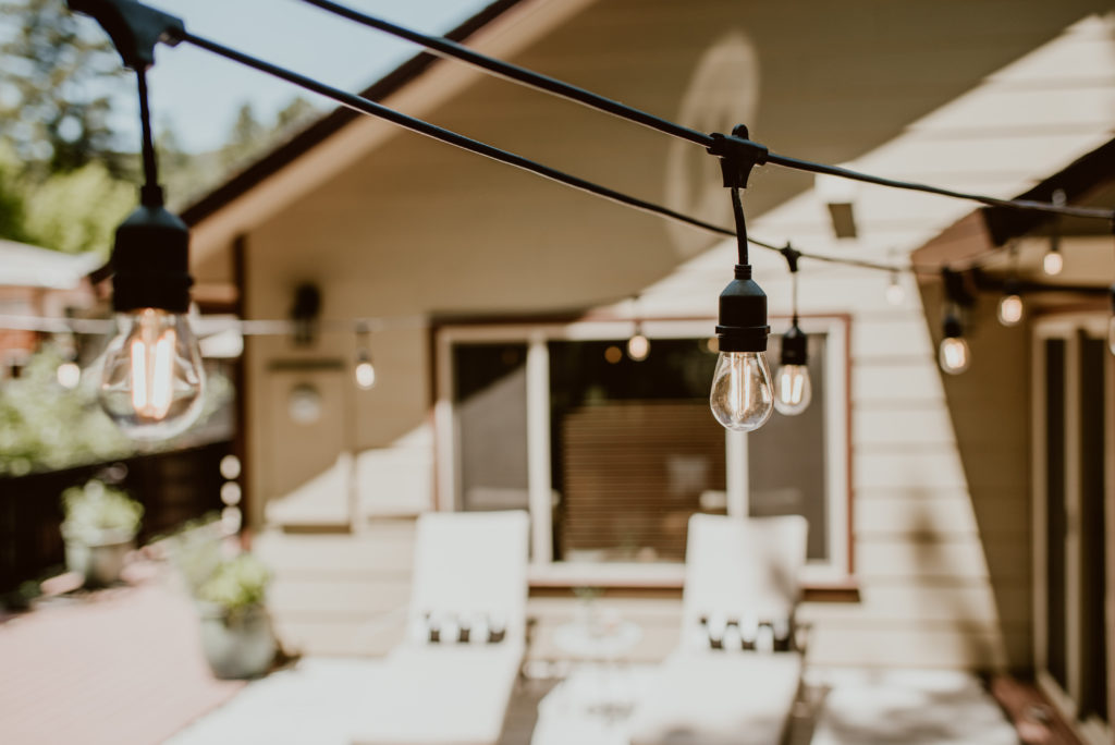 Cafe string lights hang in strands across the photo. A backyard deck is given a summer refresh.