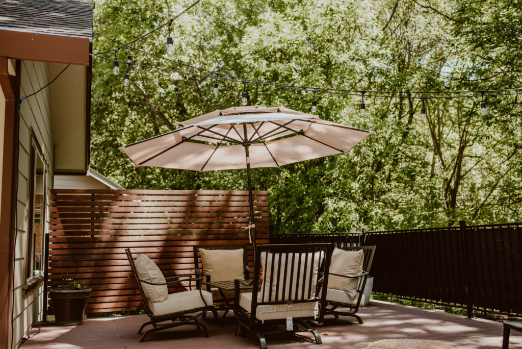 A table and chairs sit under an umbrella on a deck among the trees. A backyard deck is given a summer refresh.