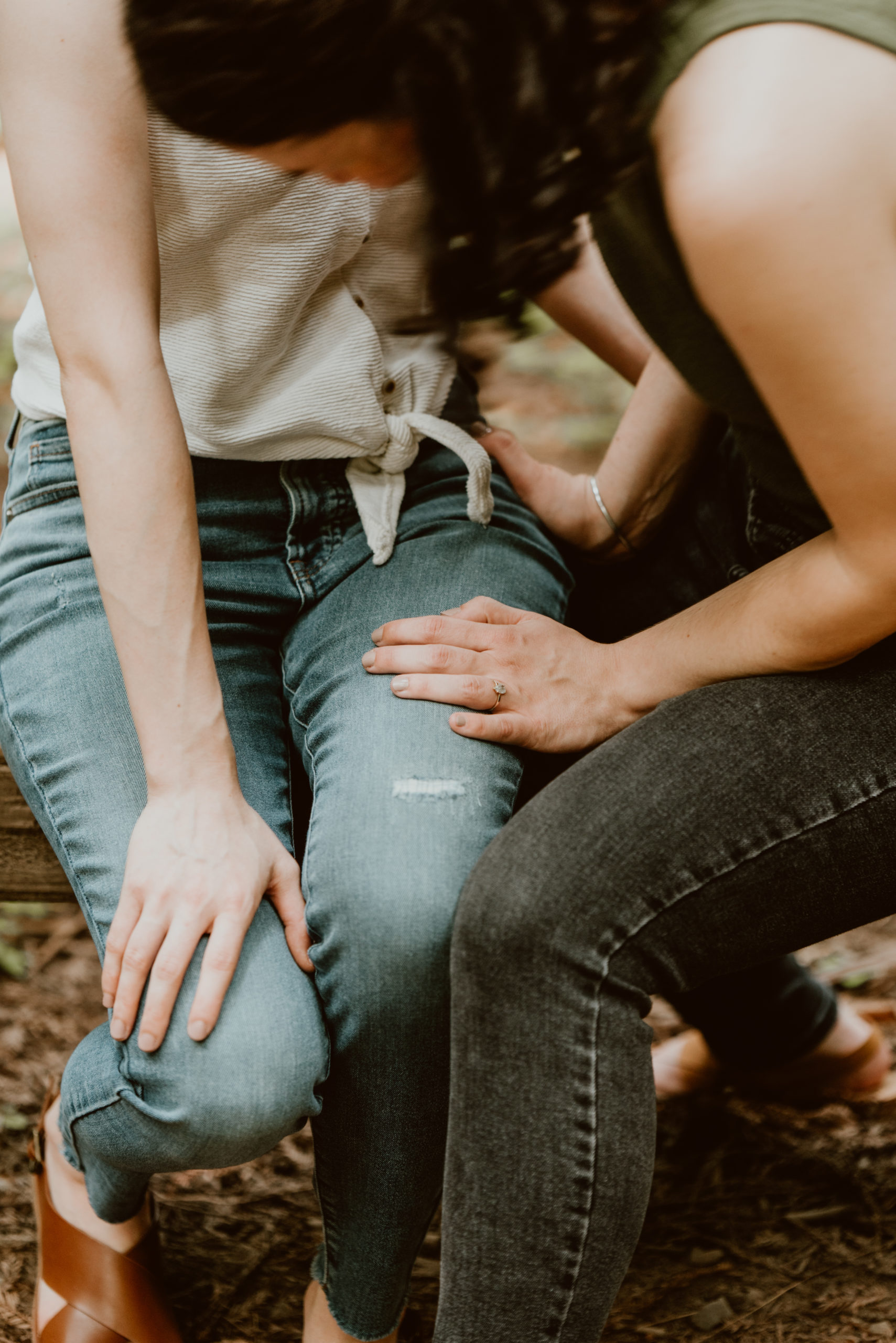 Two women sit side by side with only their legs and hands in view. Be sure to check out this post for photos from their forest and river engagement session!