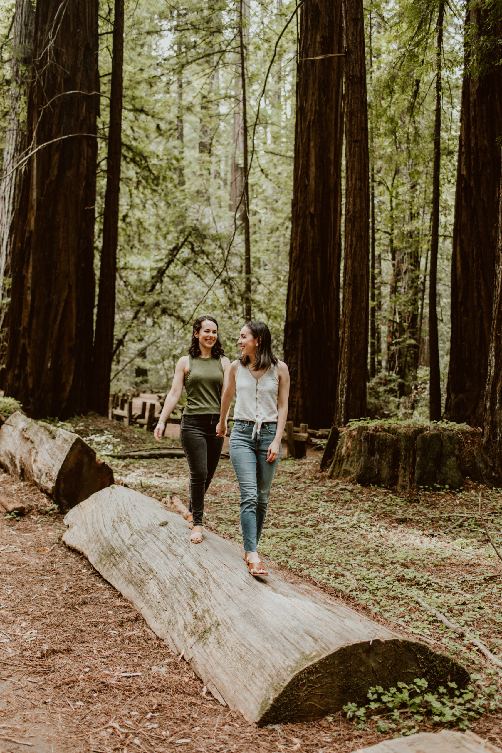 Two women walk hand in hand in the forest. Be sure to check out this post for photos from their forest and river engagement session!