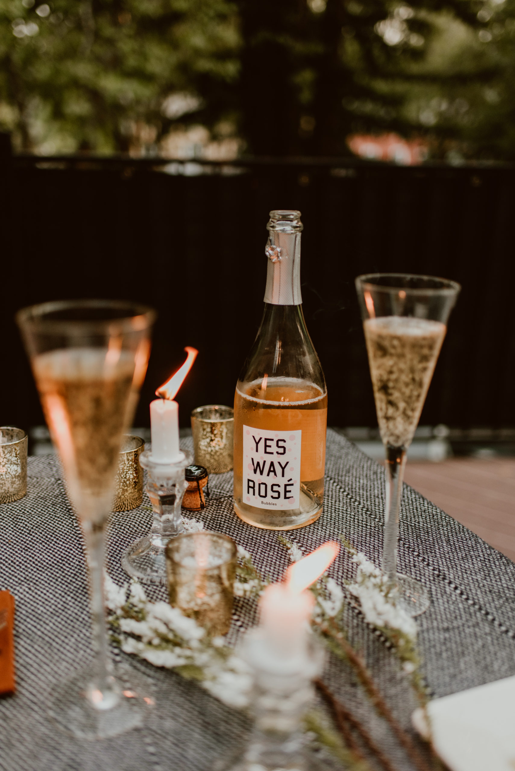Two full champagne glasses and lit candles sit on a table. Read this post for an elegant and easy way to celebrate your original wedding date.