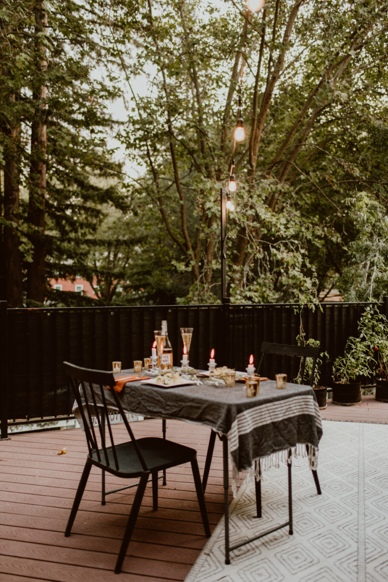 A table is set for two under a string of lights and a canopy of trees. Read this post for an elegant and easy way to celebrate your original wedding date.