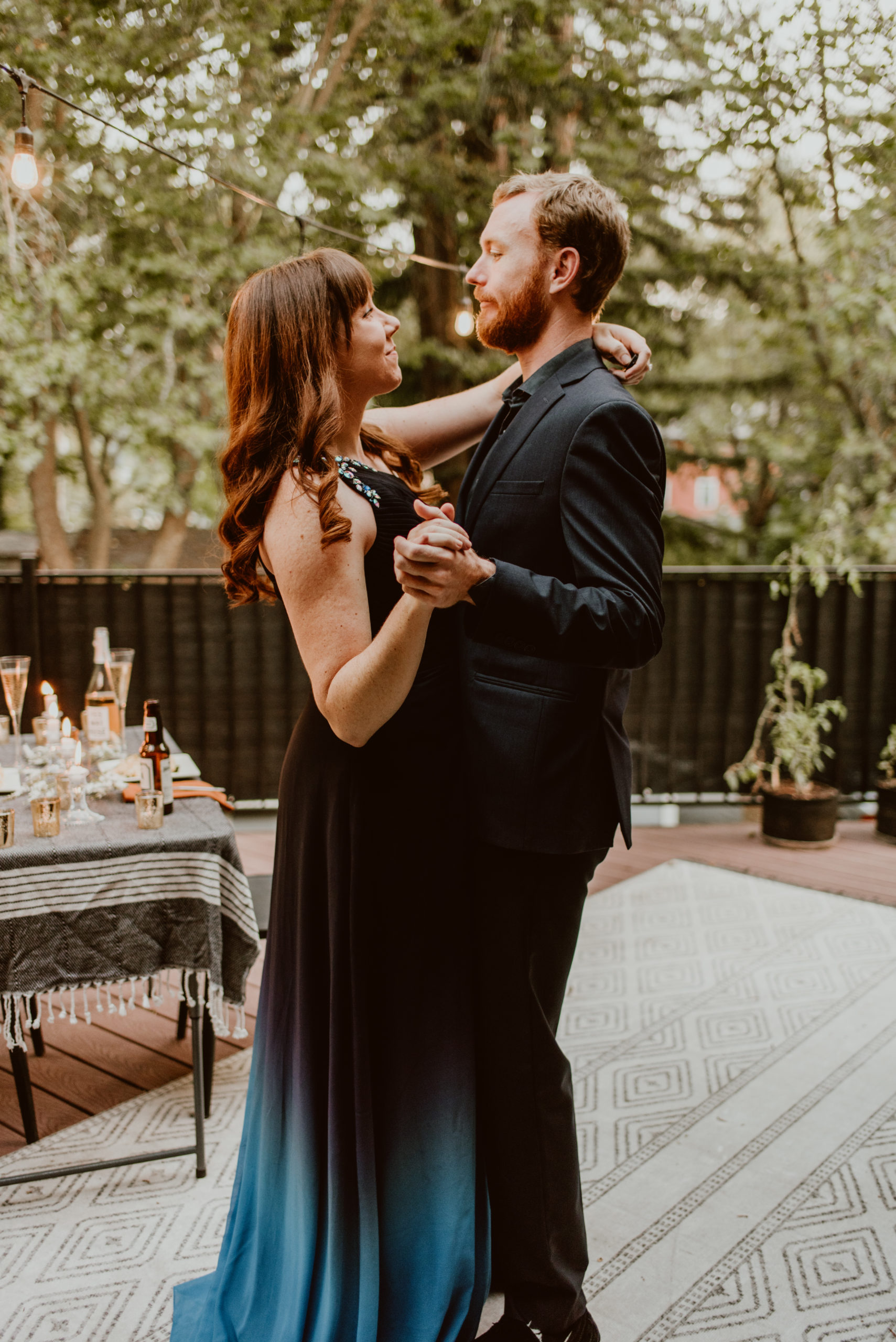 A couple in formal wear slow dances under a string of lights and a canopy of trees. Read this post for an elegant and easy way to celebrate your original wedding date.