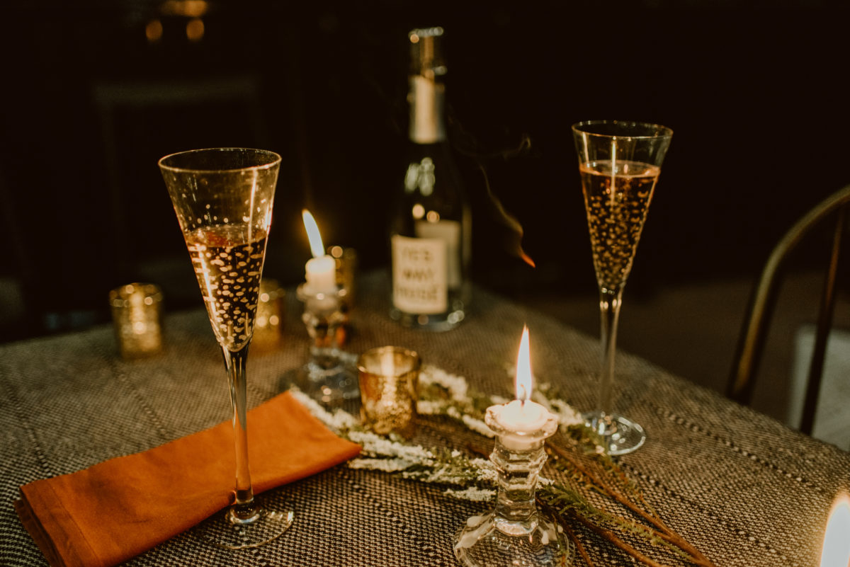 Two filled champagne glasses rest on a table at night amongst burning candles. Read this post for an elegant and easy way to celebrate your original wedding date.
