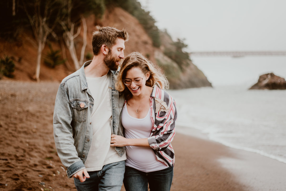 A couple walk arm in arm down a beach alone. If you're stuck wondering what to wear to your fall photo shoot, this guide has my five fave outfit items for your session!
