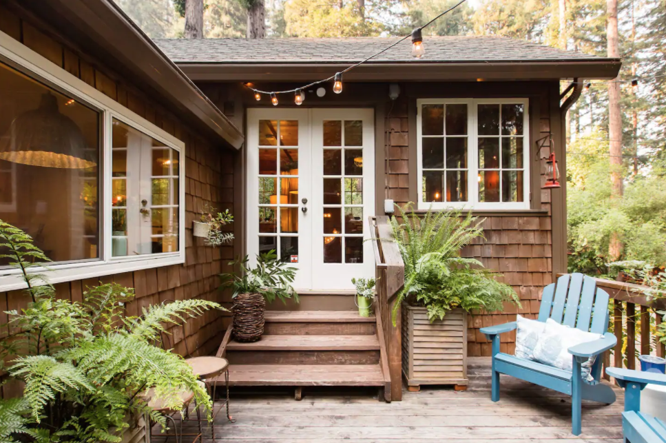 A brown wood shingle house sits in the forest with ferns and Adirondack chairs set beside the front door, with string lights overhead.  If you're going to elope in NorCal and still need a place to stay, look no further. Here are nine of my favorite Russian River elopement Airbnb's you won't be able to choose between!
