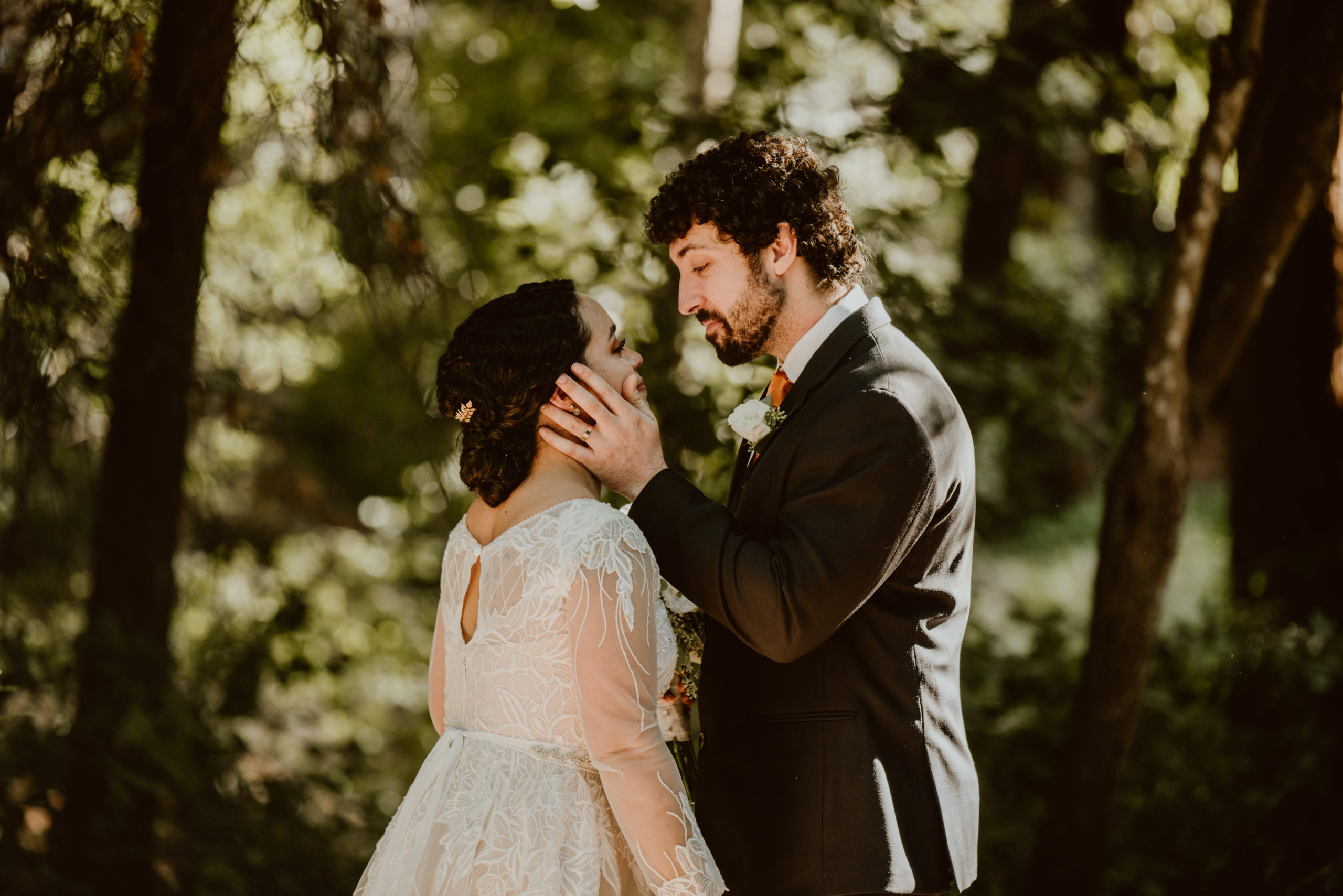 A groom holds his bride's face as he leans down to kiss her in front of a sunny grove of trees. This page details what an elopement is and why you should have one, so be sure to give it a read if you're curious about them!