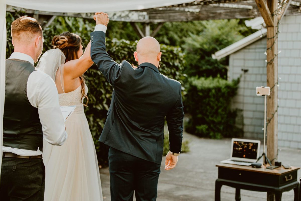 A just-married bride and groom raise their clasped hands in celebration, with a laptop open in the background displaying their friends and family on the video call.

If you're currently grappling with making a Plan B or even Plan C because of covid, this backyard elopement in wine country will help give you some inspo!