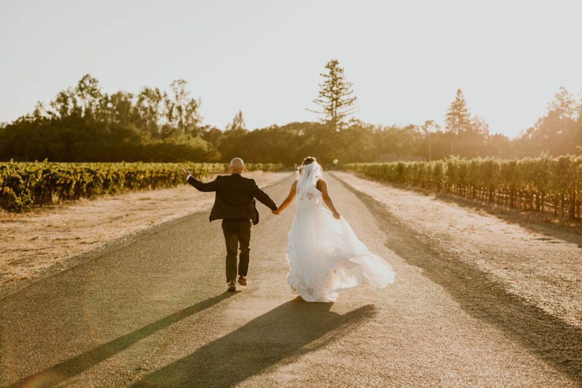 A bride and groom jog down a road in the vineyards towards the sunset. They are both grinning at the camera.

If you're currently grappling with making a Plan B or even Plan C because of covid, this backyard elopement in wine country will help give you some inspo!