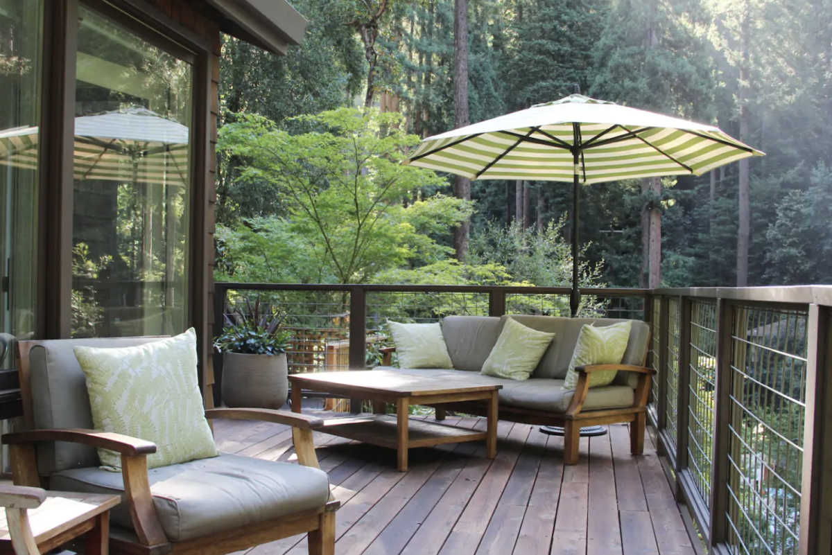 An outdoor couch, armchair, and umbrella sit on a deck overlooking a forest.  If you're going to elope in NorCal and still need a place to stay, look no further. Here are nine of my favorite Russian River elopement Airbnb's you won't be able to choose between!