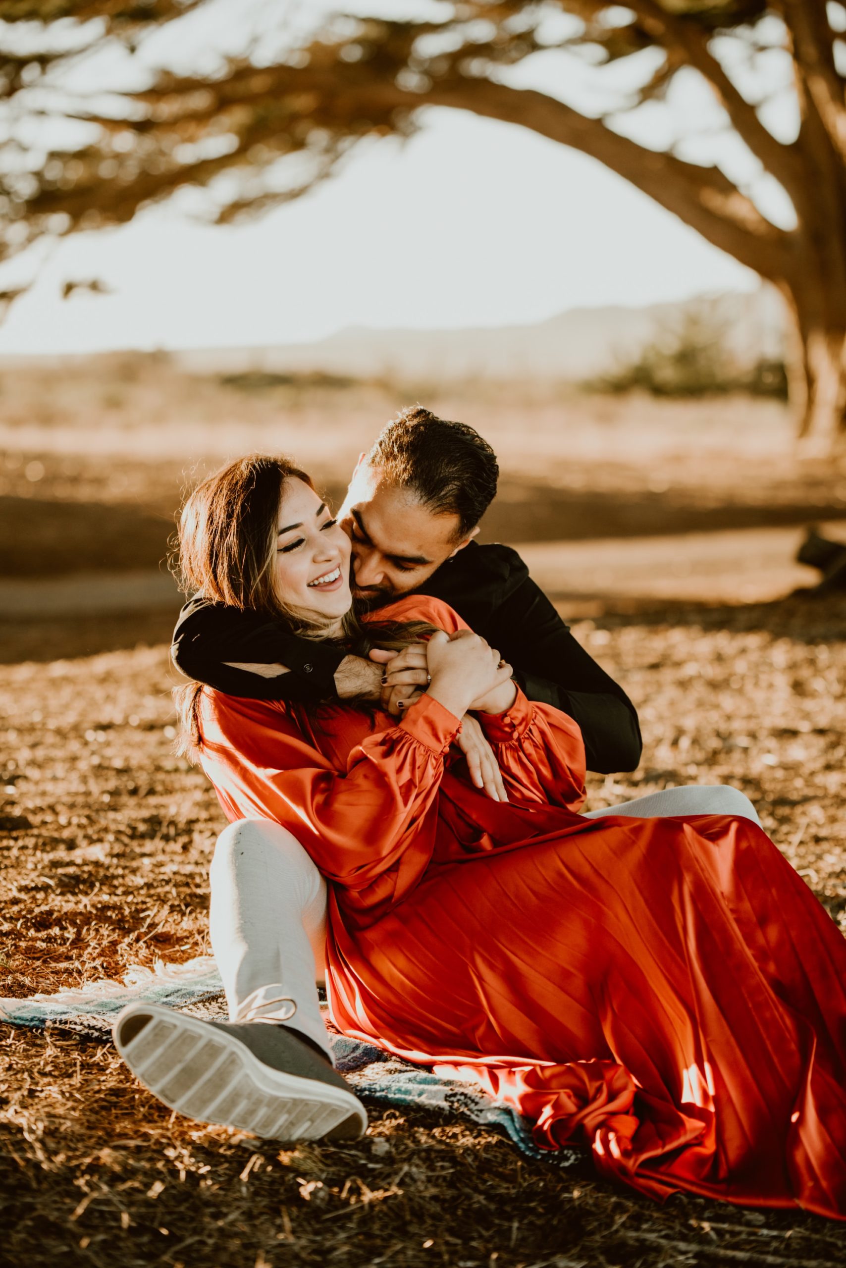 A woman sits between the legs of a man while they embrace and laugh under the Cypress Tree Tunnel during their Point Reyes engagement session.