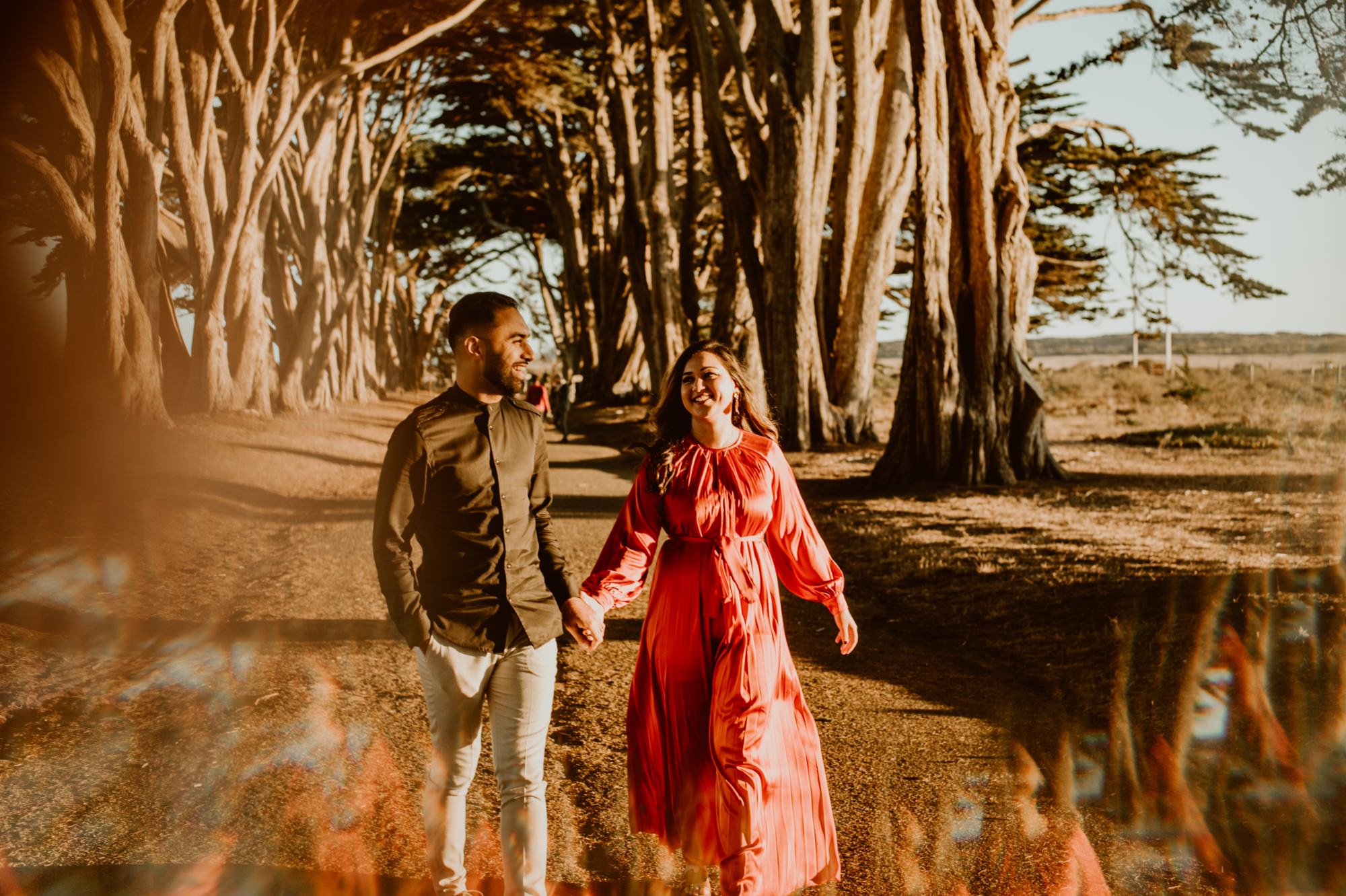 A man and woman run toward the camera while holding hands in the sunlight under the Cypress Tree Tunnel during their Point Reyes engagement session.