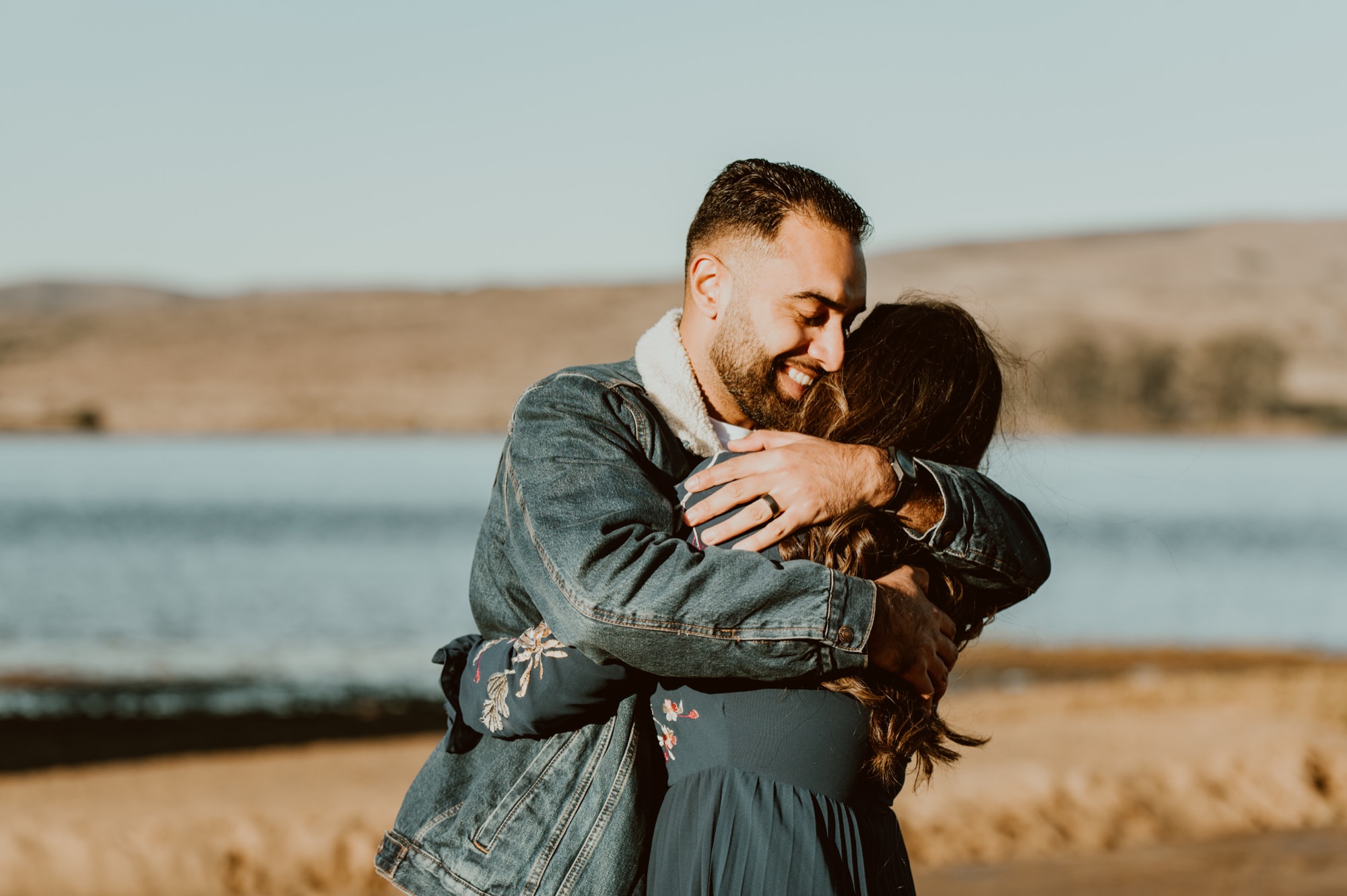 A man and woman embrace while smiling and swaying back in forth in front of Tomales Bay during their Point Reyes engagement session.