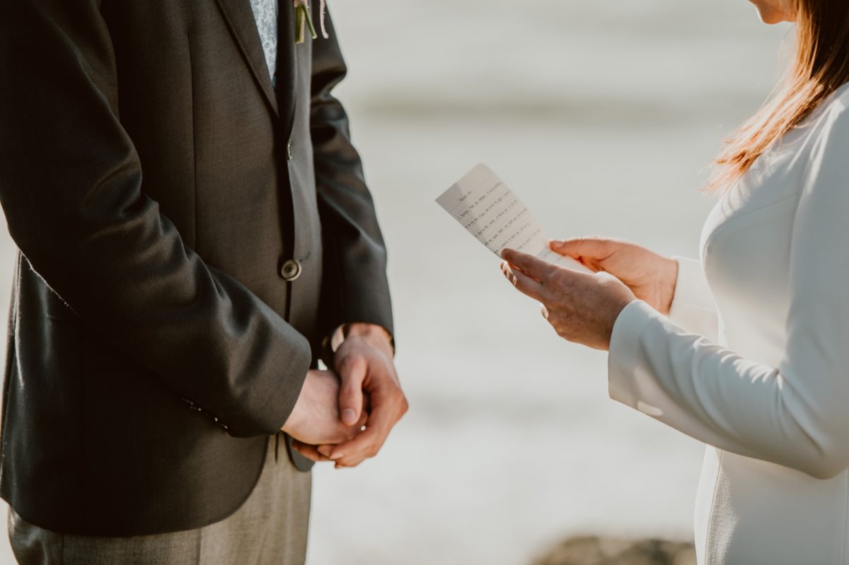 A woman holds her wedding vows in both hands and reads them aloud to her husband during their wedding ceremony on the Sonoma coast.