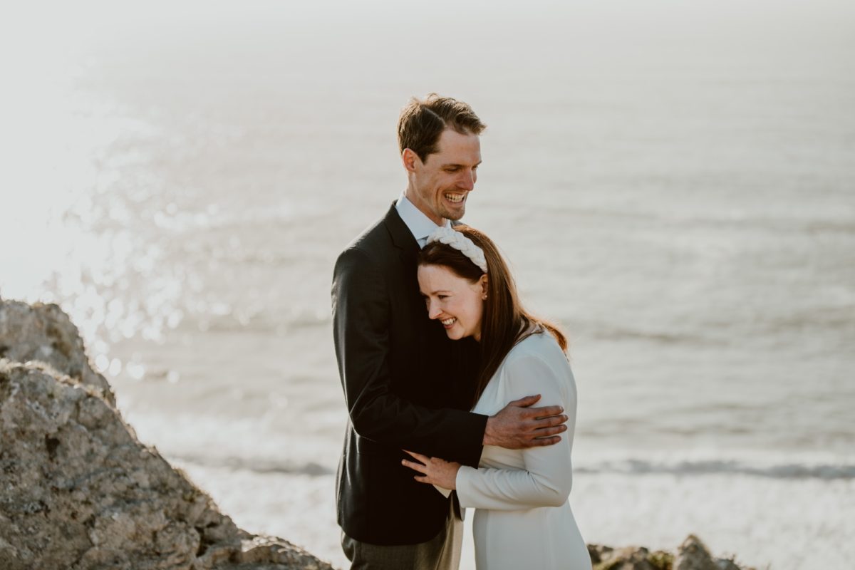 A man and woman embrace with a laugh during their wedding ceremony on the Sonoma coast.