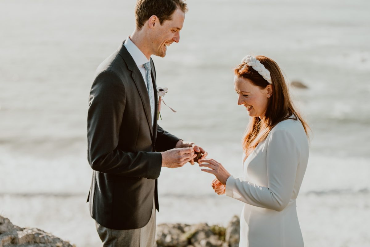 A man is about to place a ring on the hand of his wife during their wedding ceremony on the Sonoma coast.