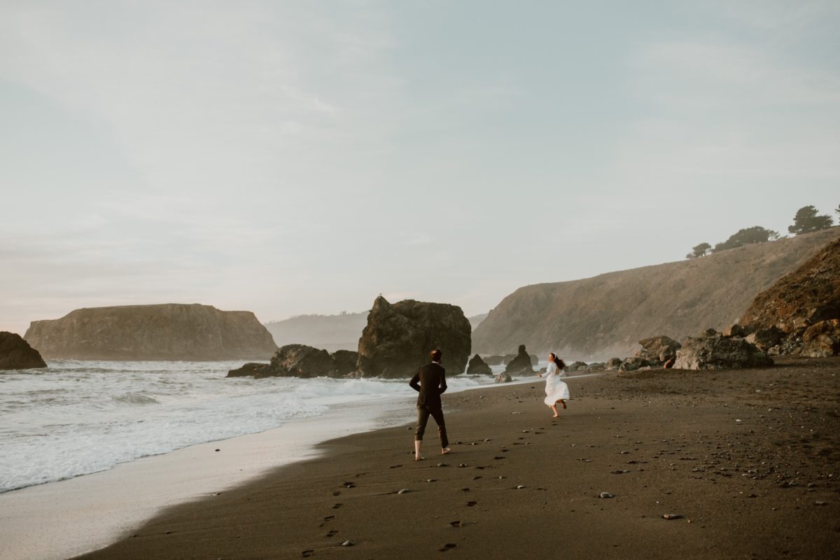A couple run laughing along the beach on their elopement day on the Sonoma coast.