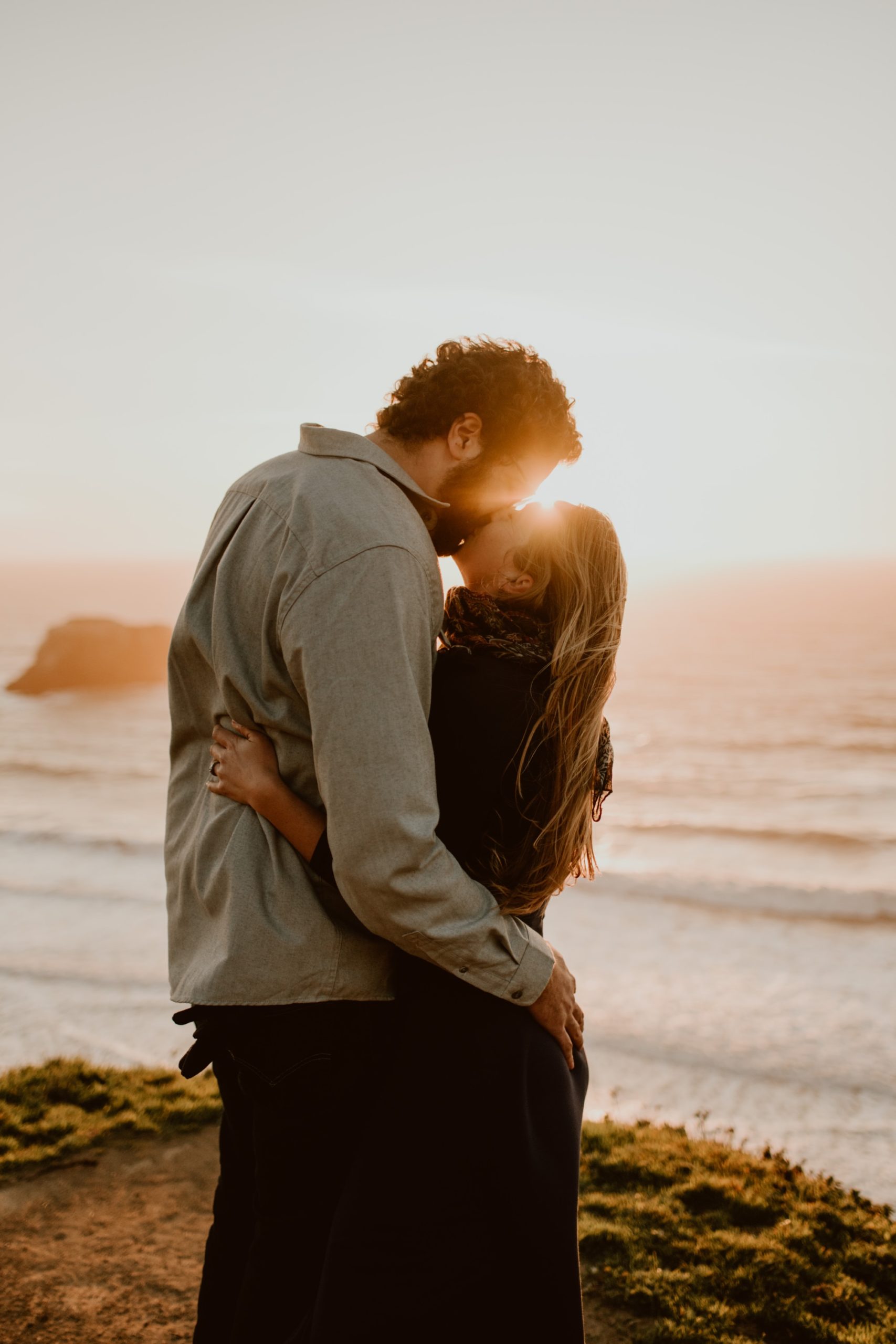 A couple embrace and share a kiss on the Sonoma coast at sunset.
