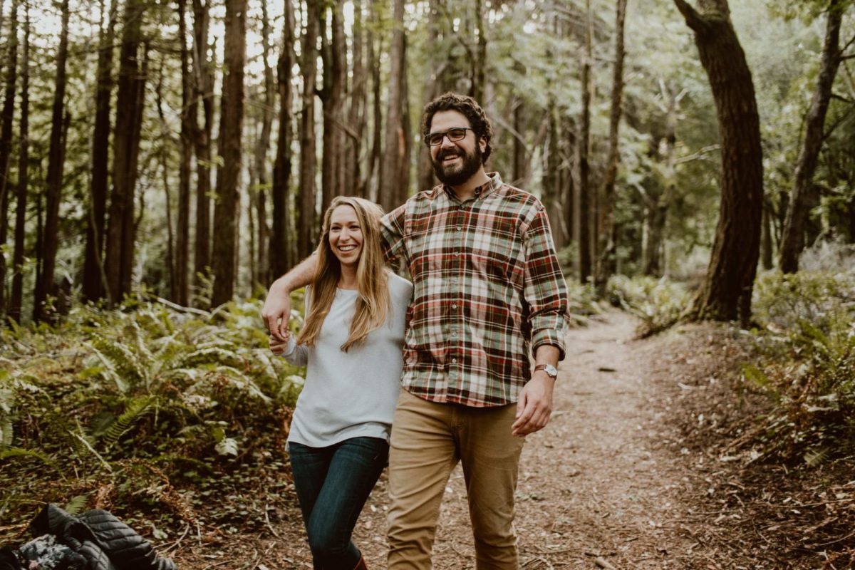 A couple walks with arms around each other down a trail in a redwood forest on the Sonoma coast.